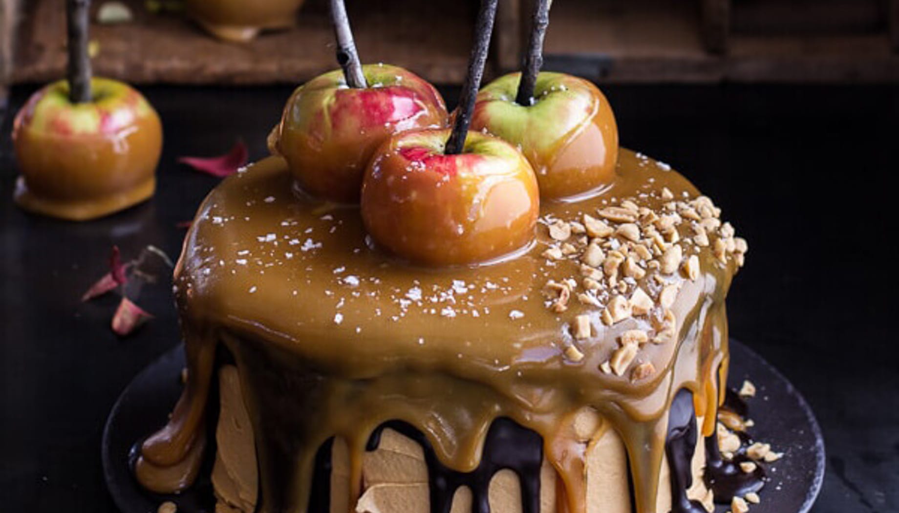 salted-caramel-apple-snickers-cake Cake with gooey caramel flowing over the edges and caramel apples on top.